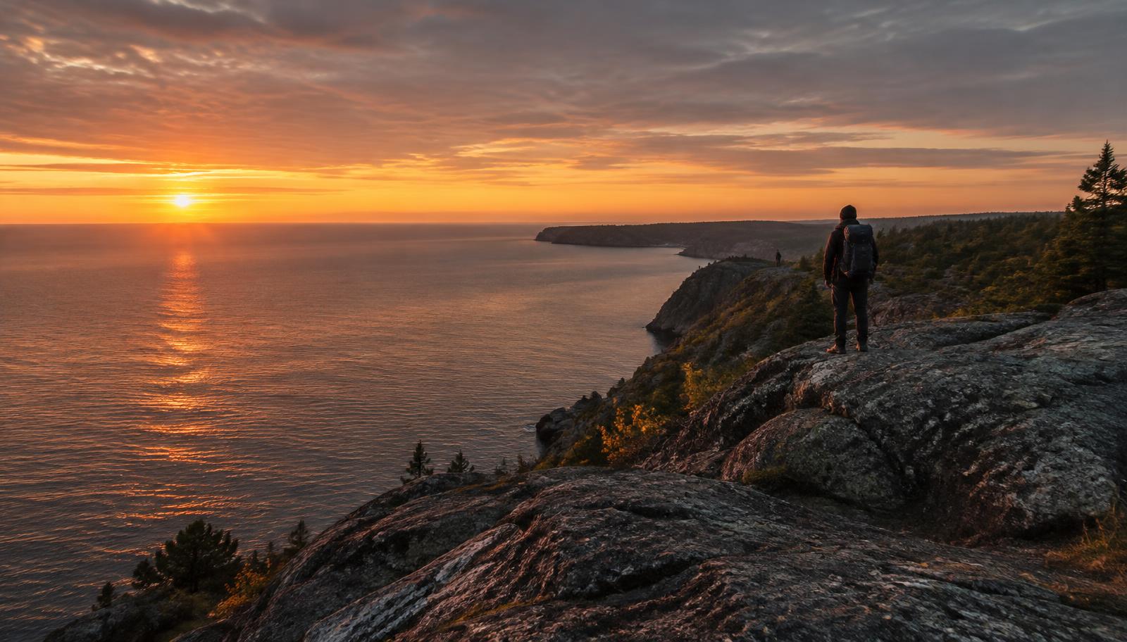 A hiker standing on a rocky Lake Superior ridge at sunset
